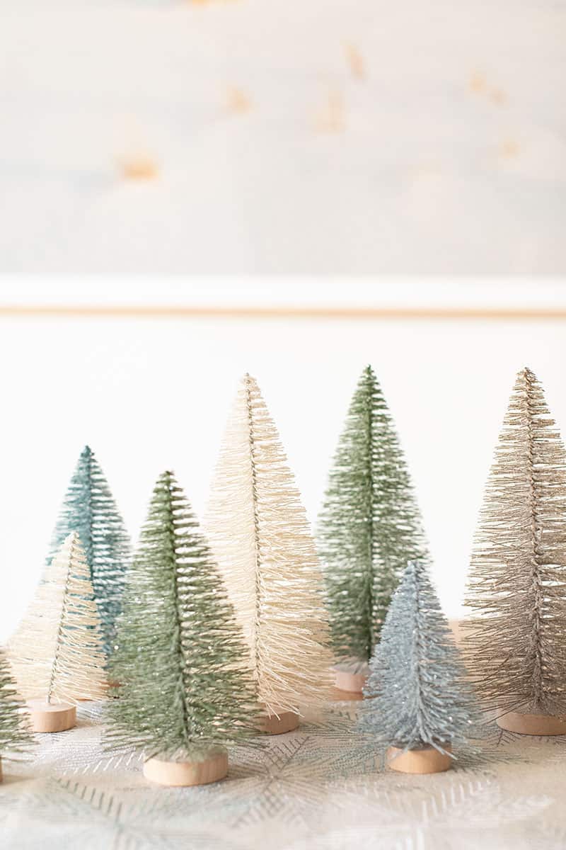 Blue, green and white bottle brush Christmas trees on a table. 