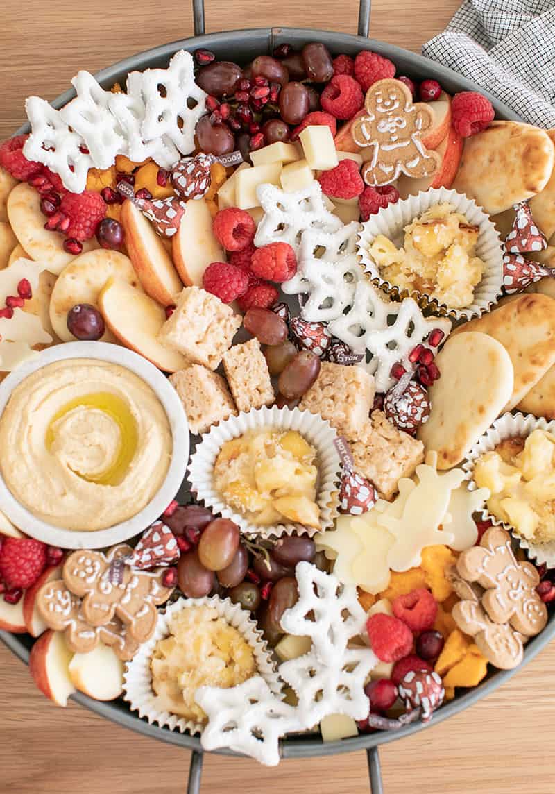 A round tray filled with Christmas Appetizers for Kids. Hummus, cheese, berries, cookies. 