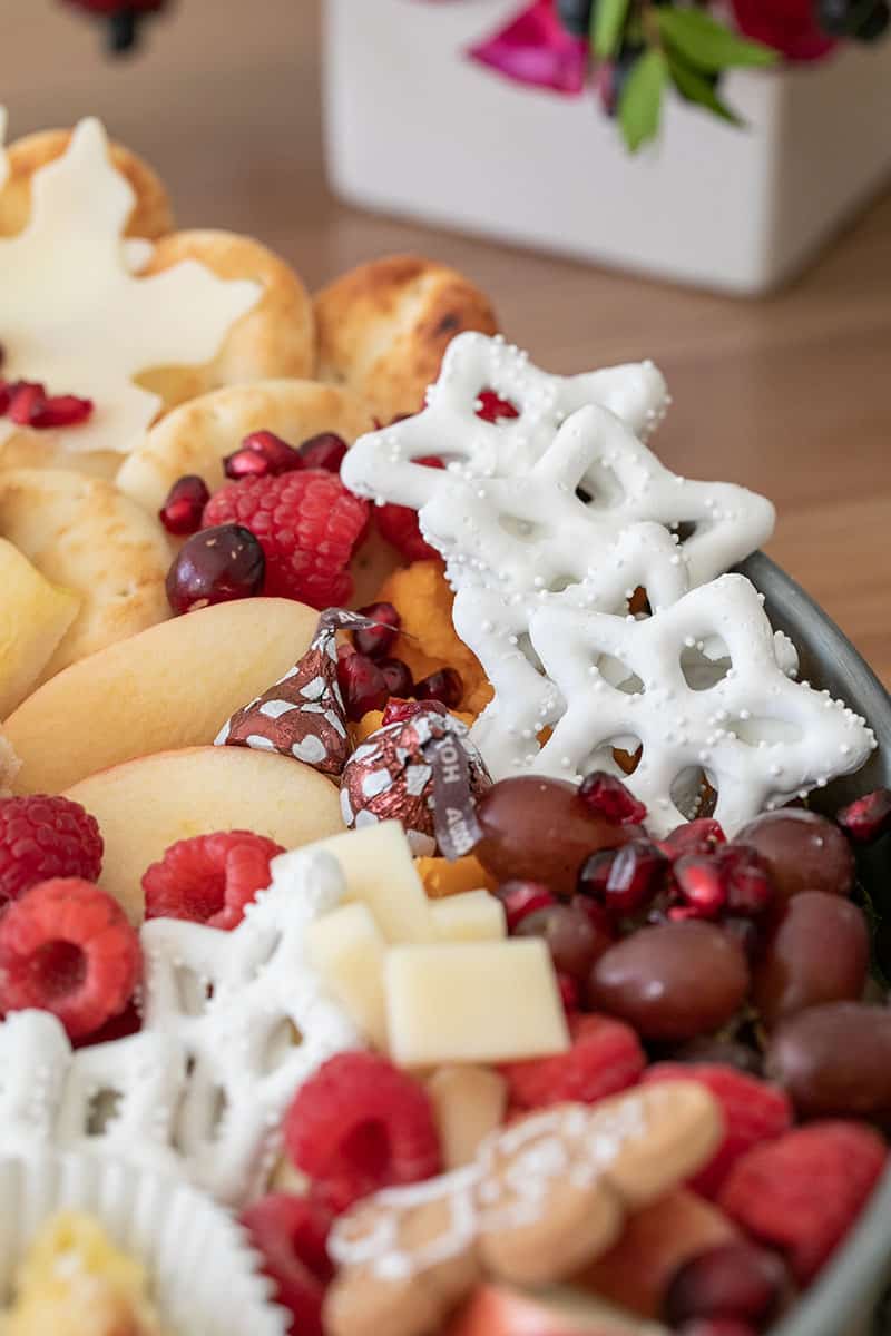 Yogurt covered pretzels, grapes, cheese, apples and pita bread on a round tray. 