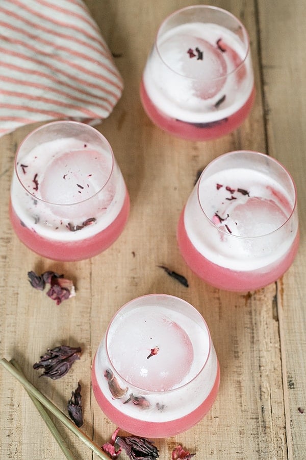 Hibiscus gin sour on a wooden table in a glass with a round ice cube. - valentine's day cocktails