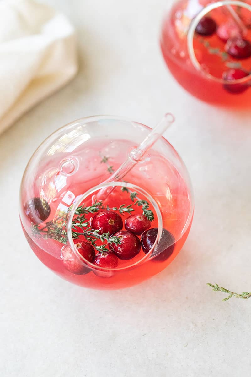 Cranberry gin and tonic in a round glass with fresh cranberries and thyme. 