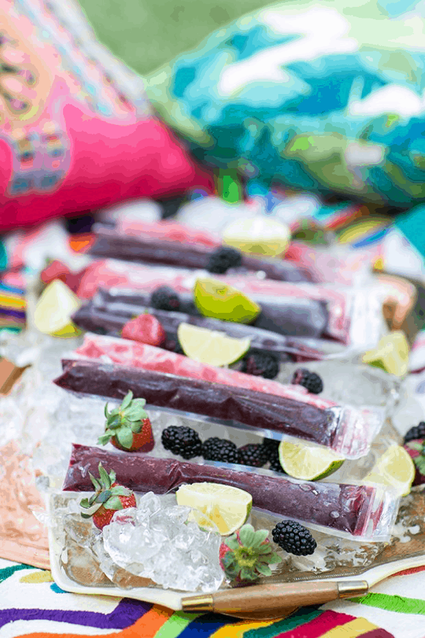 Frozen margarita popsicles in pouches with limes and berries on a tray.