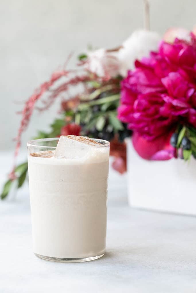 A creamy white Sicilian kiss cocktail with cinnamon and hot pink flowers in the back.