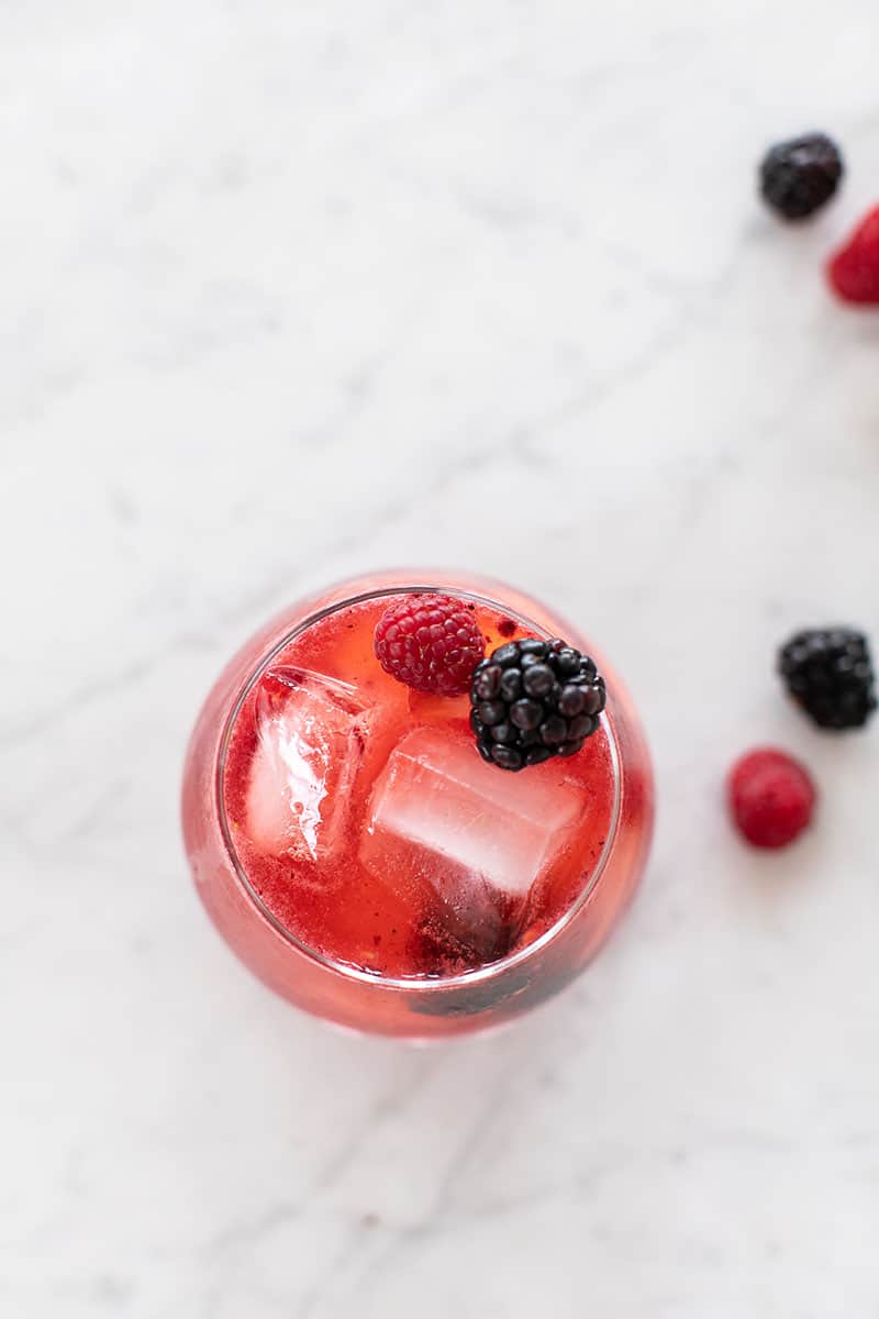 Red cocktail with blackberries and raspberries and ice cubes on a marble table.