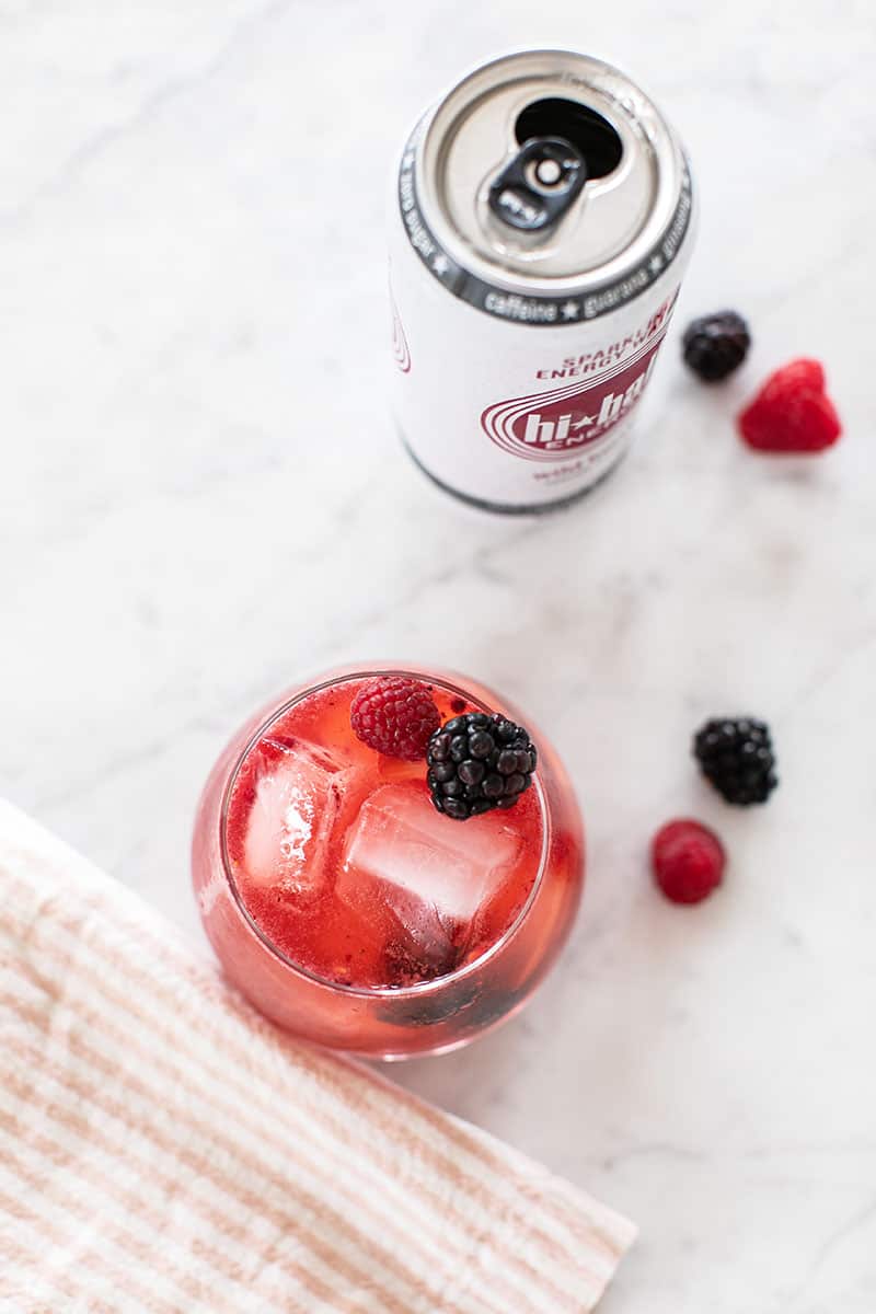 Festive red cocktail with berries and a pink napkin and a can of Hiball energy water.
