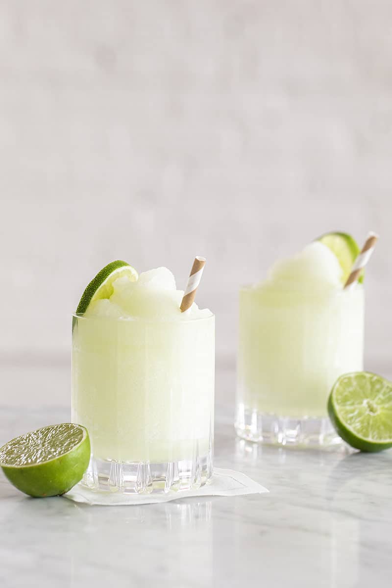 Frozen cocktail in an old fashioned glass with lime slice and paper straw.