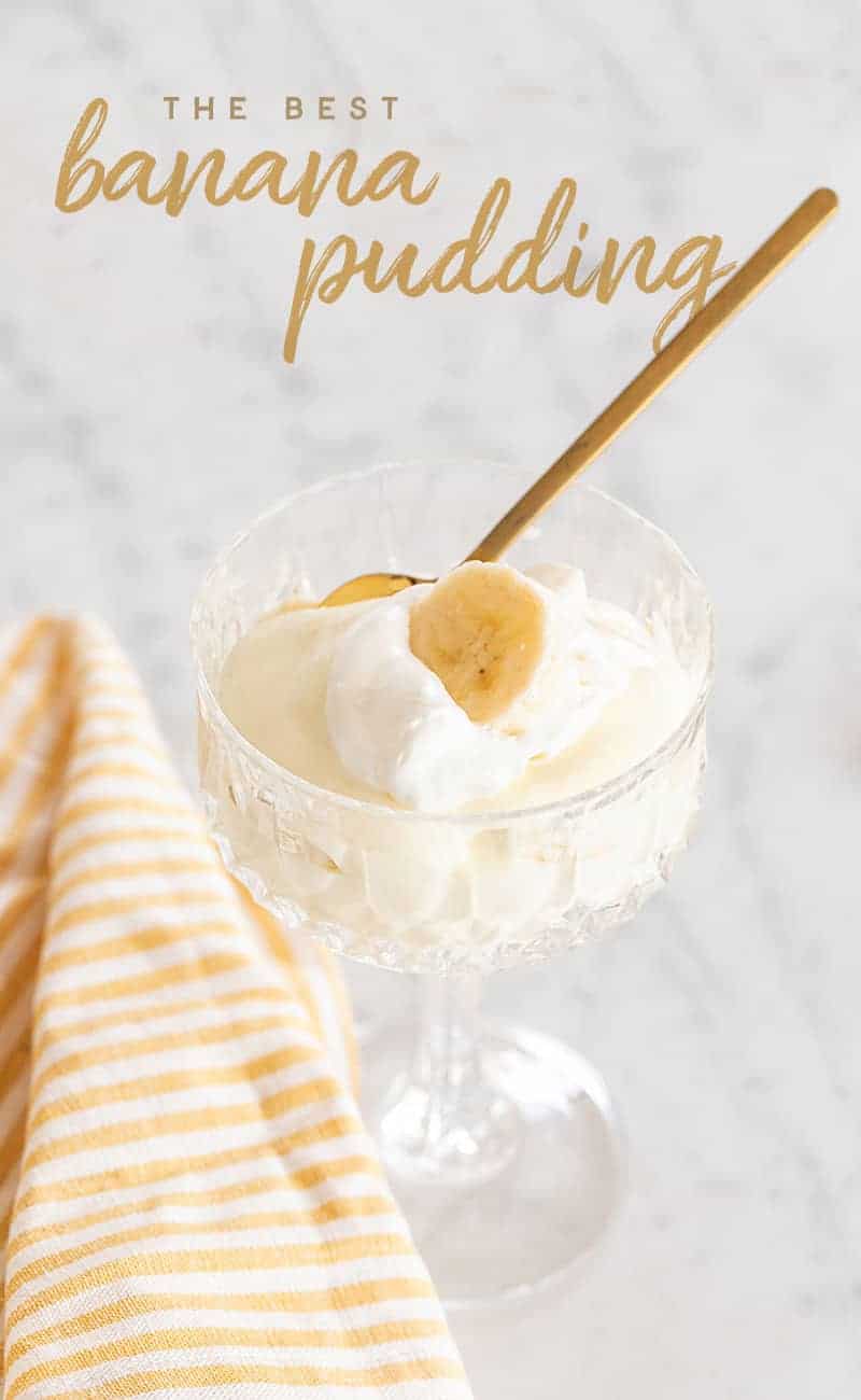 Banana pudding in a glass with a gold spoon with a striped yellow towel.