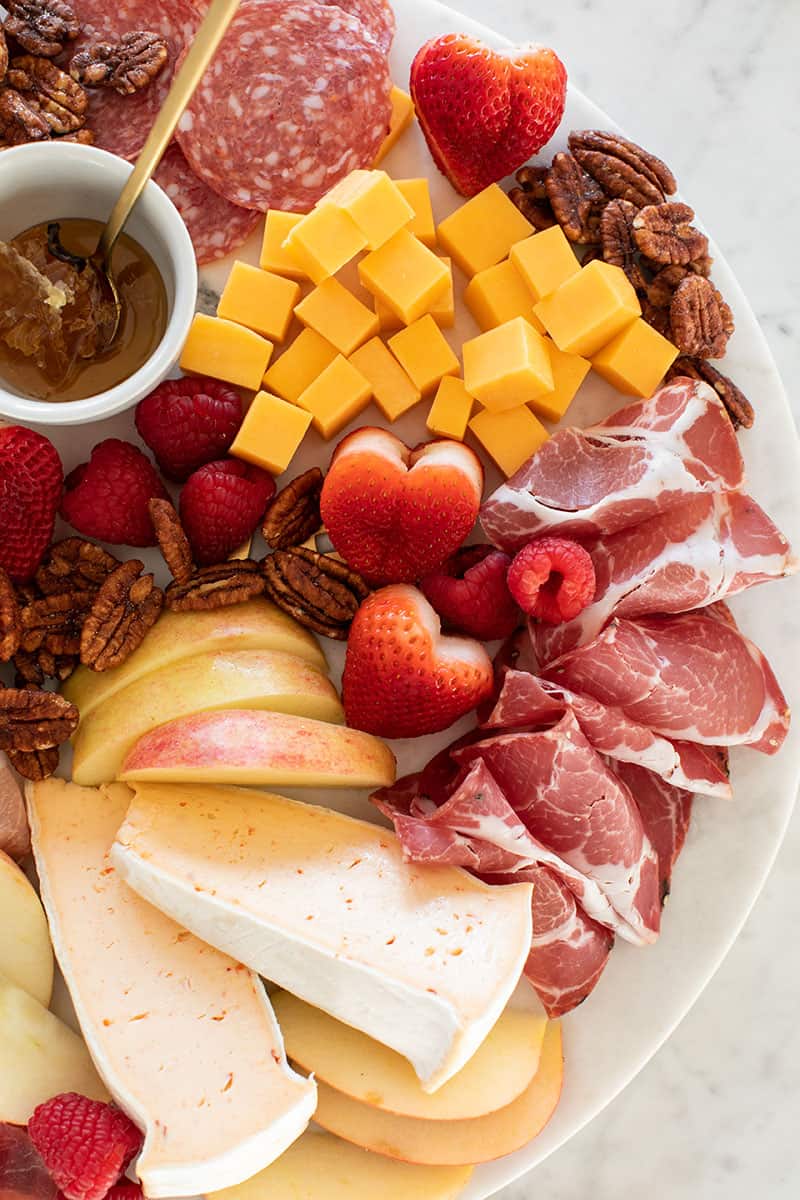 Meat and cheese on a board with heart shaped strawberries