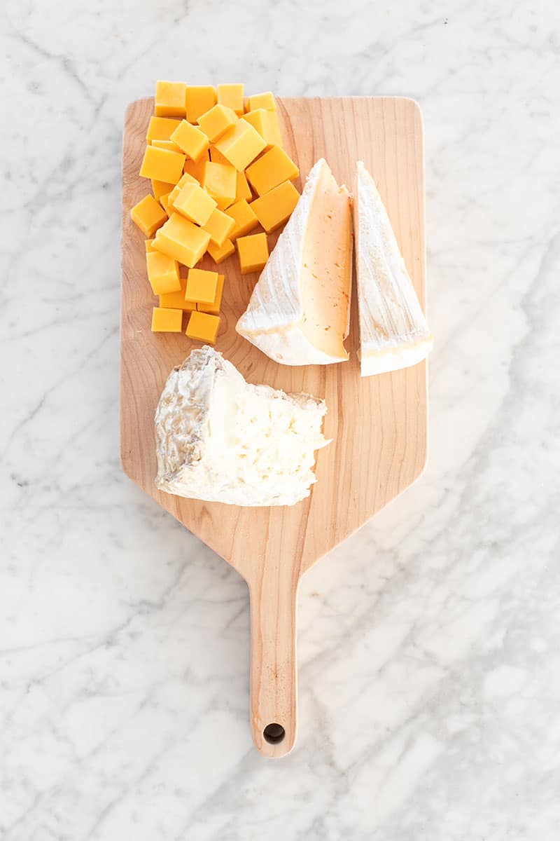 Three types of cheese on a wooden board.