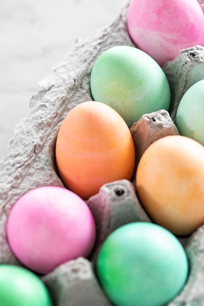 Orange, green and pink dyed Easter eggs in a carton.