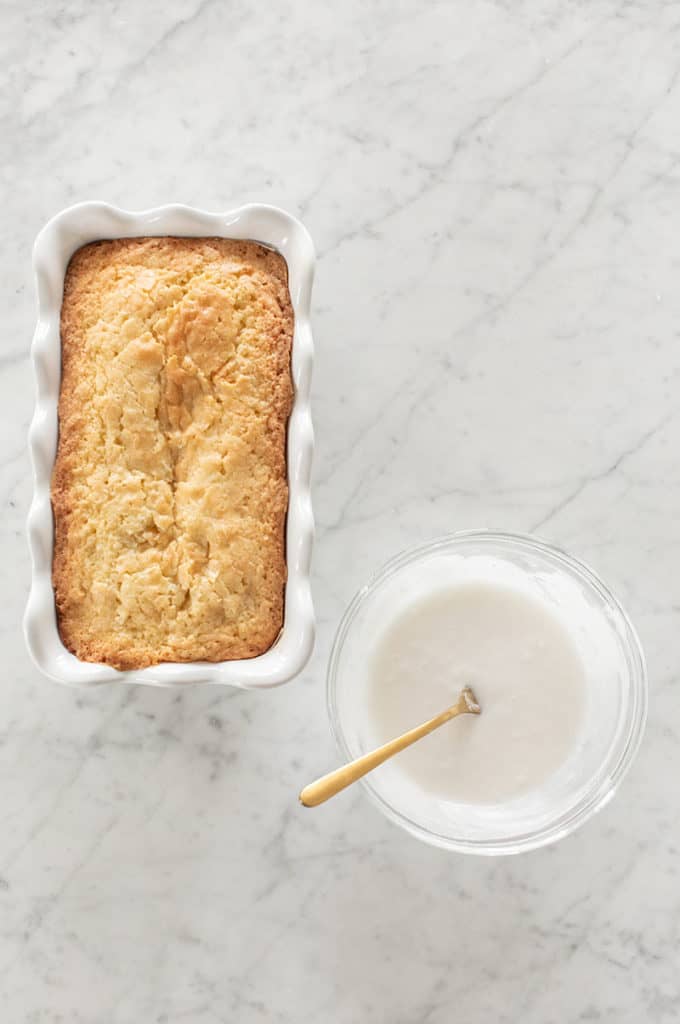 Coconut loaf cake and glaze on a marble table.