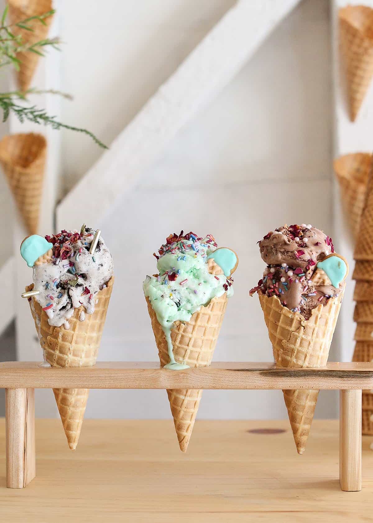 Three colorful ice cream cones in a wooden cone holder with sprinkles on the top of them.