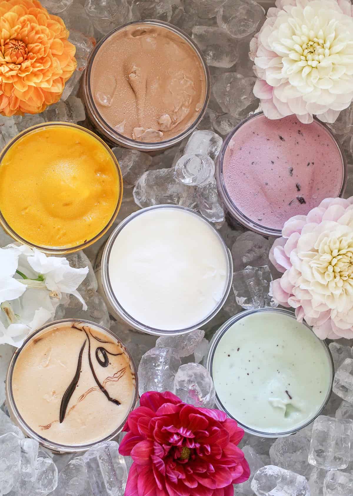 Small jars of ice cream, all different colors sitting in ice with flowers. 