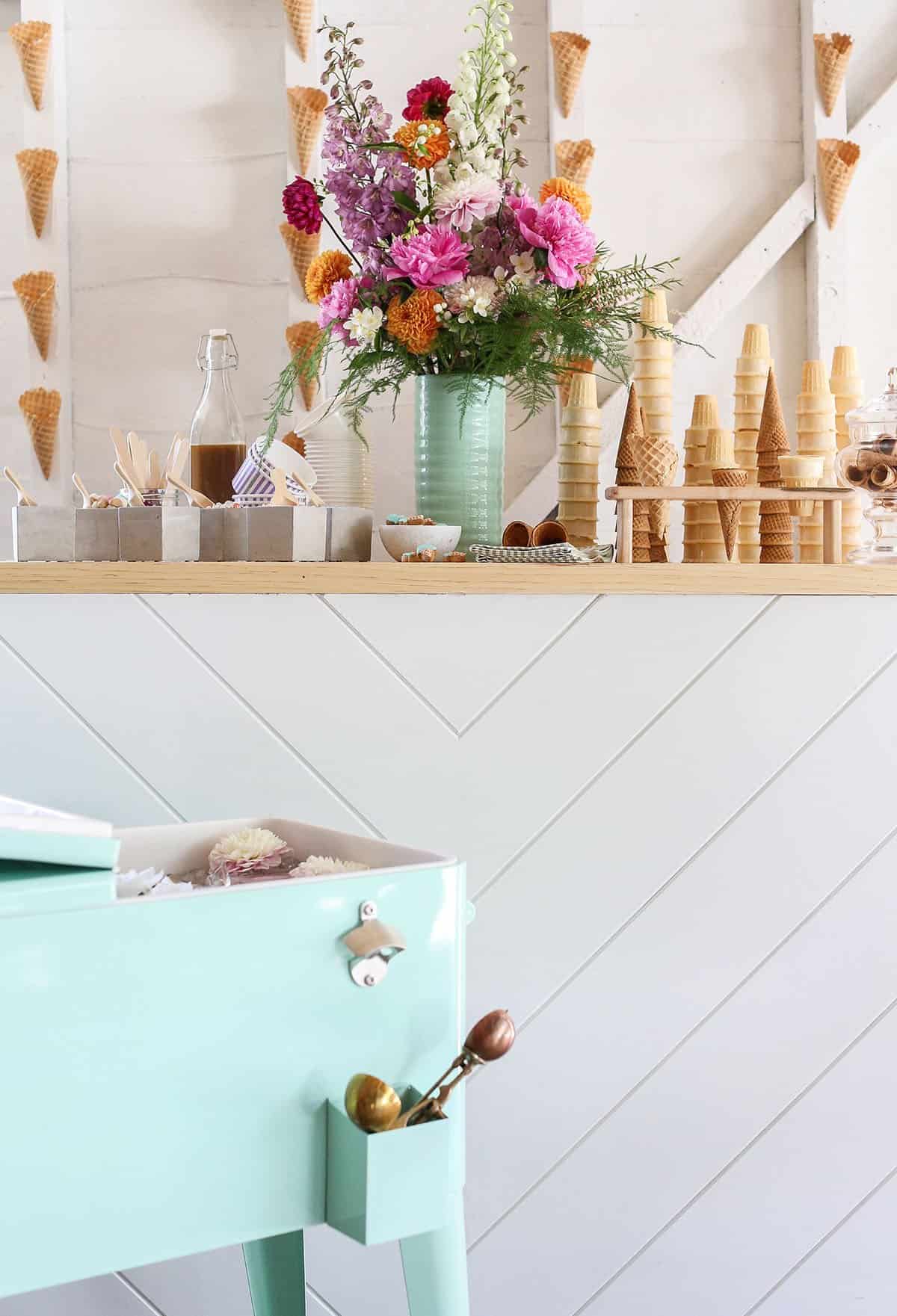 Ice cream bar with pink flowers and a green cooler with ice cream tubs.