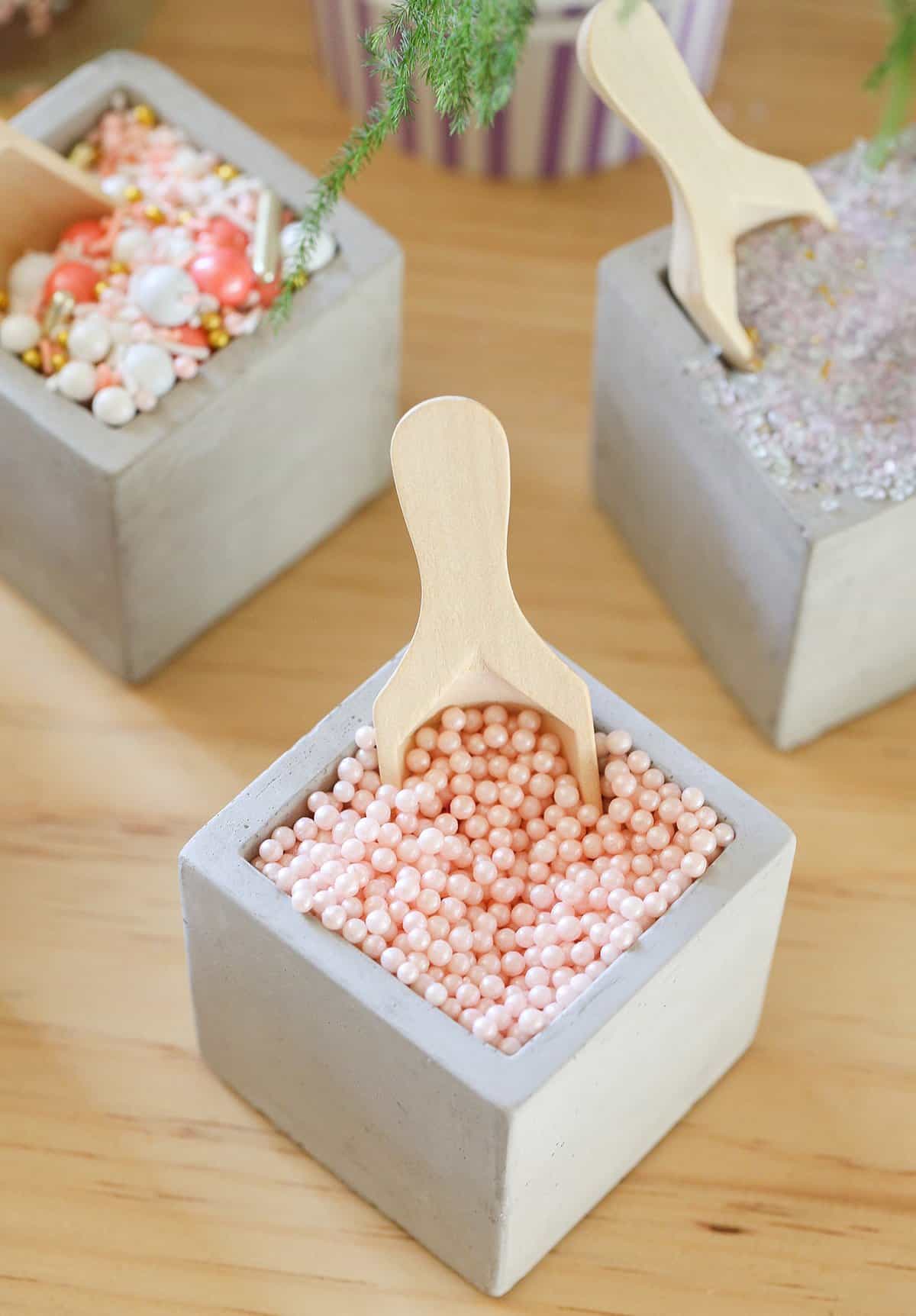 Fancy sprinkles in bowls with a small wooden scooper.