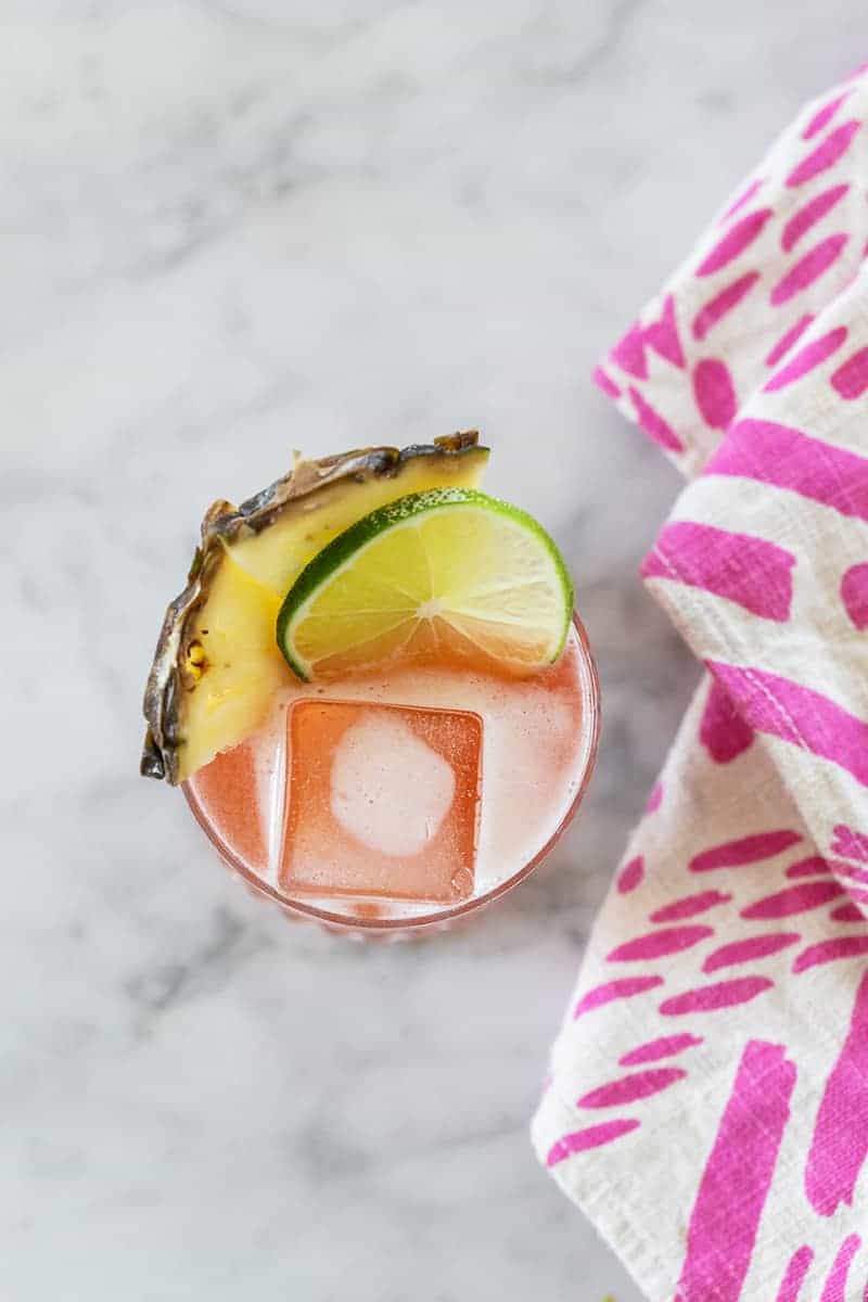 Overhead photo of a jungle bird cocktail garnished with lime and pineapple and a pink napkin. 