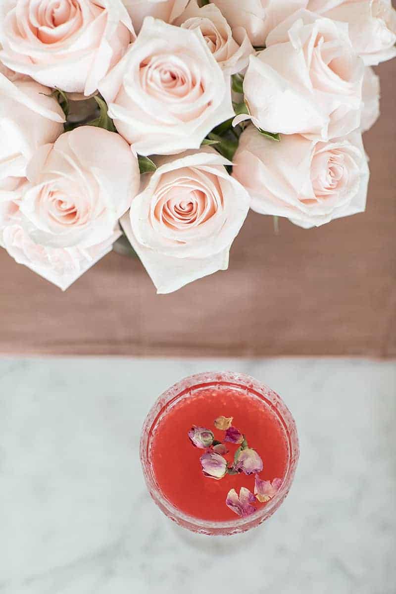 Red cocktail with dried rose petals with pink roses. 