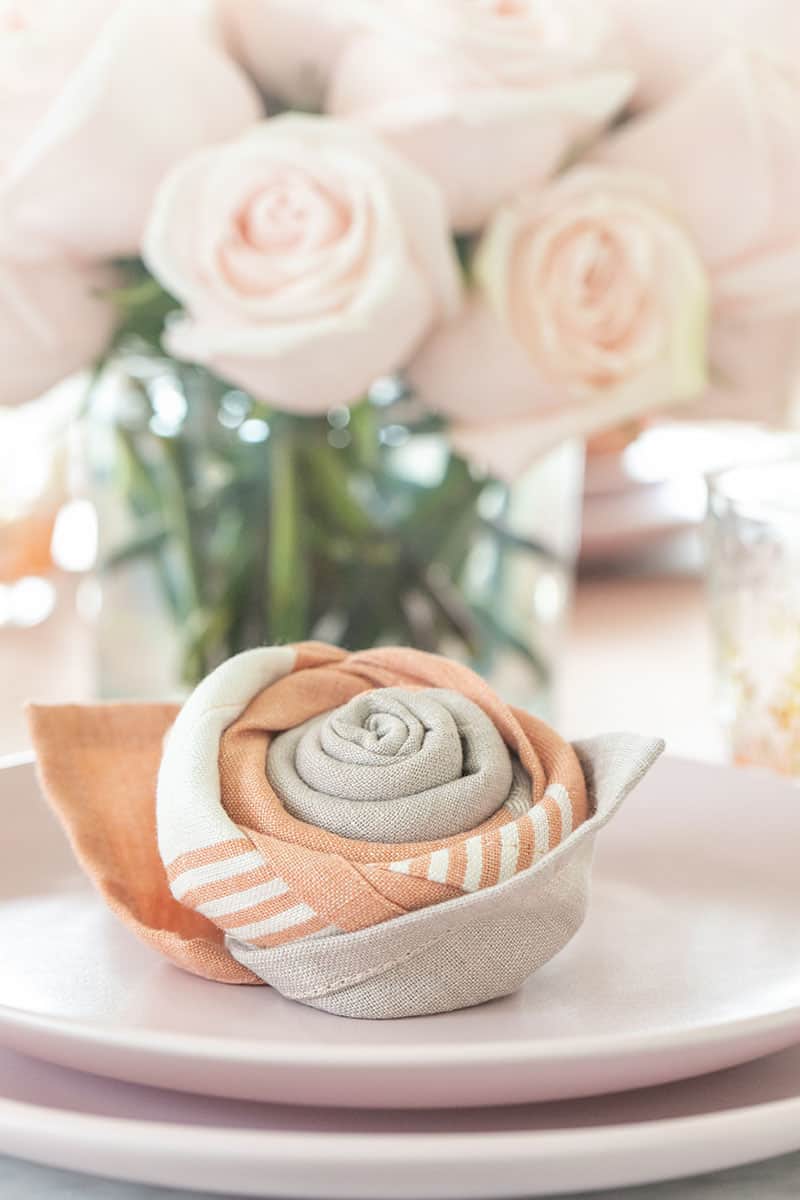 Rose napkin fold on a pink plate with pink roses.