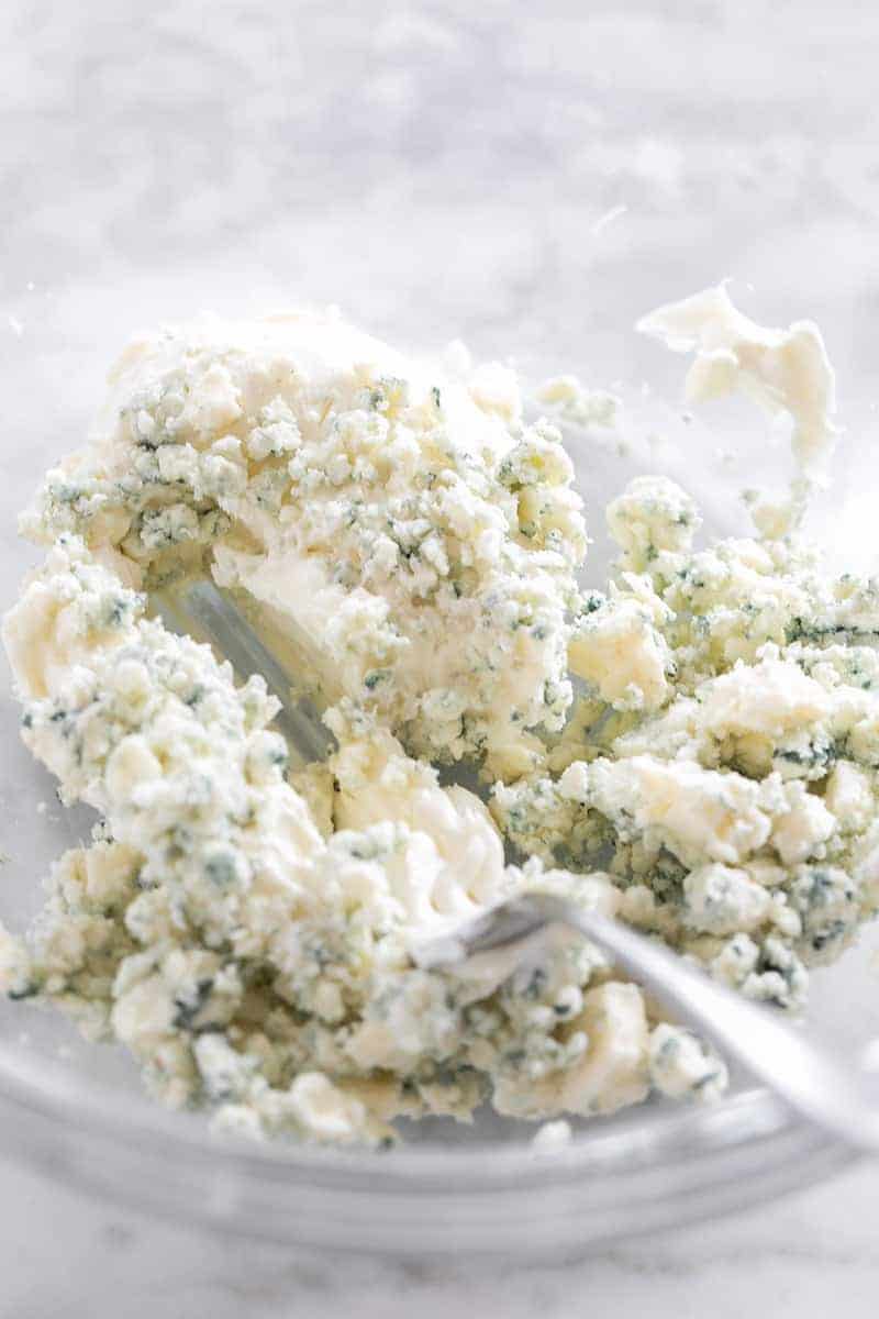 Blue cheese, cream cheese and mayonnaise being mixed in a bowl.