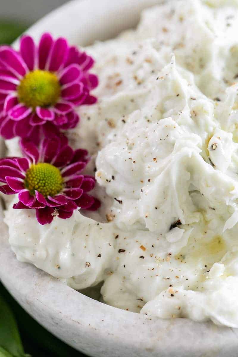 Close up photos of blue cheese dip with a little pepper and purple flowers.