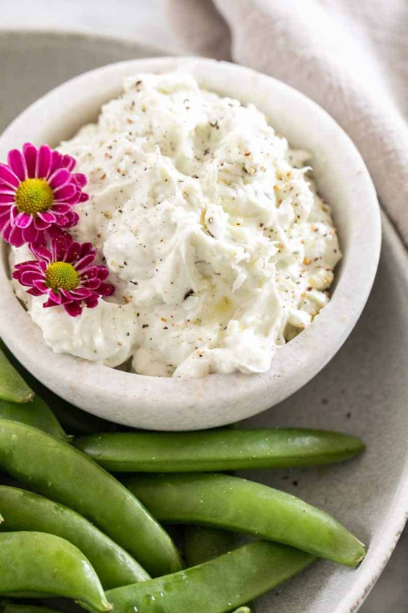 A small bowl filled with blue cheese dip garnished with flowers and a side of peas.