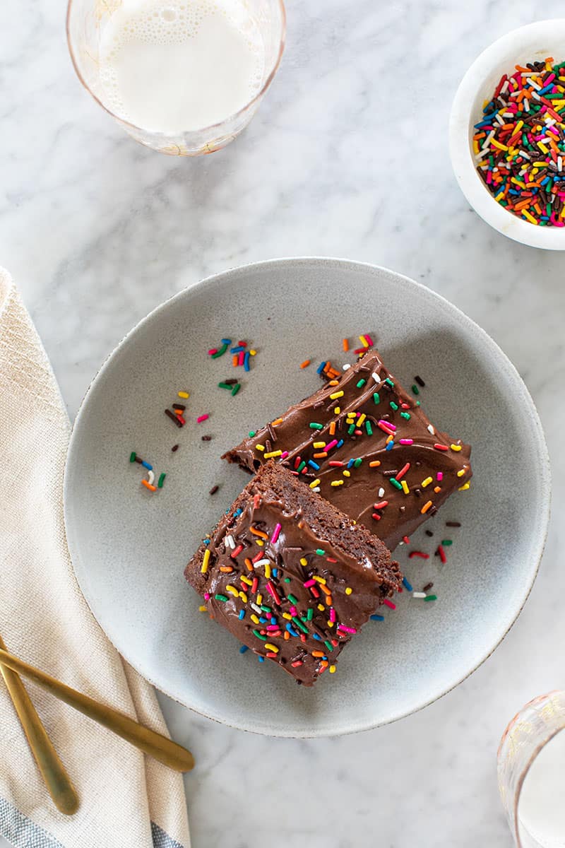 two chocolate brownies on a plate with sprinkles.