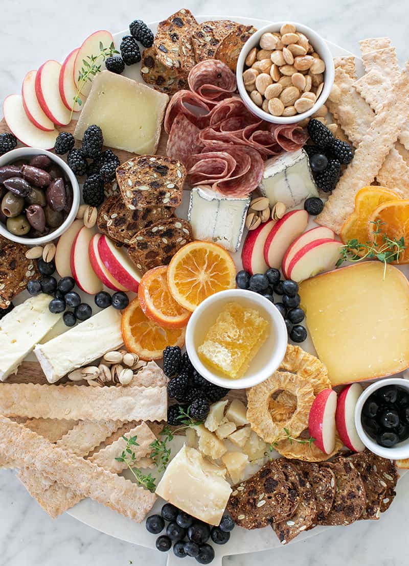 cheese platter with meat, cheese, nuts, berries and crackers.