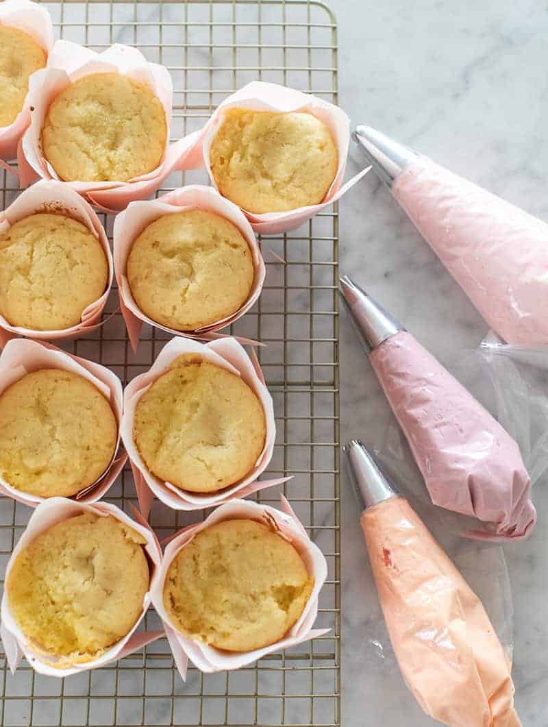 yellow cupcakes and three bags of colored buttercream frosting in piping bags.