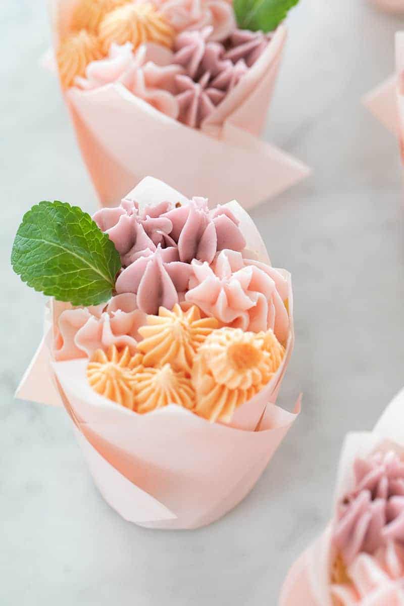 A cupcake decorated with small flowers and a tiny mint leaf.