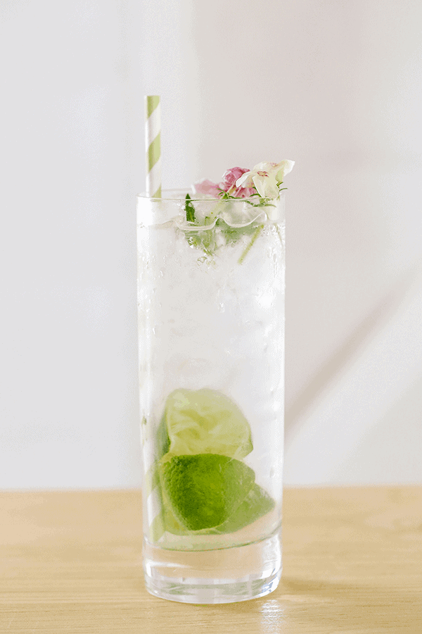 Gin and tonic cocktail in a tall glass with limes and flowers.