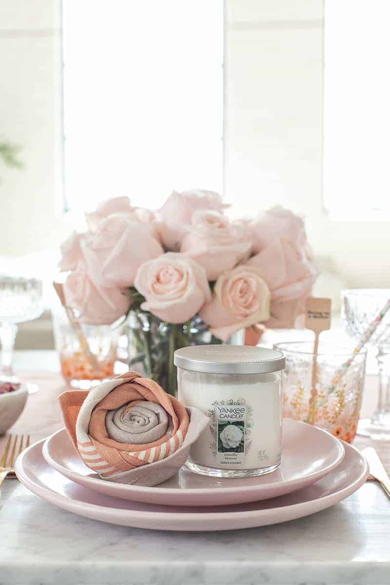 Table setting with a Yankee candle and rose napkin fold with pink flowers. 