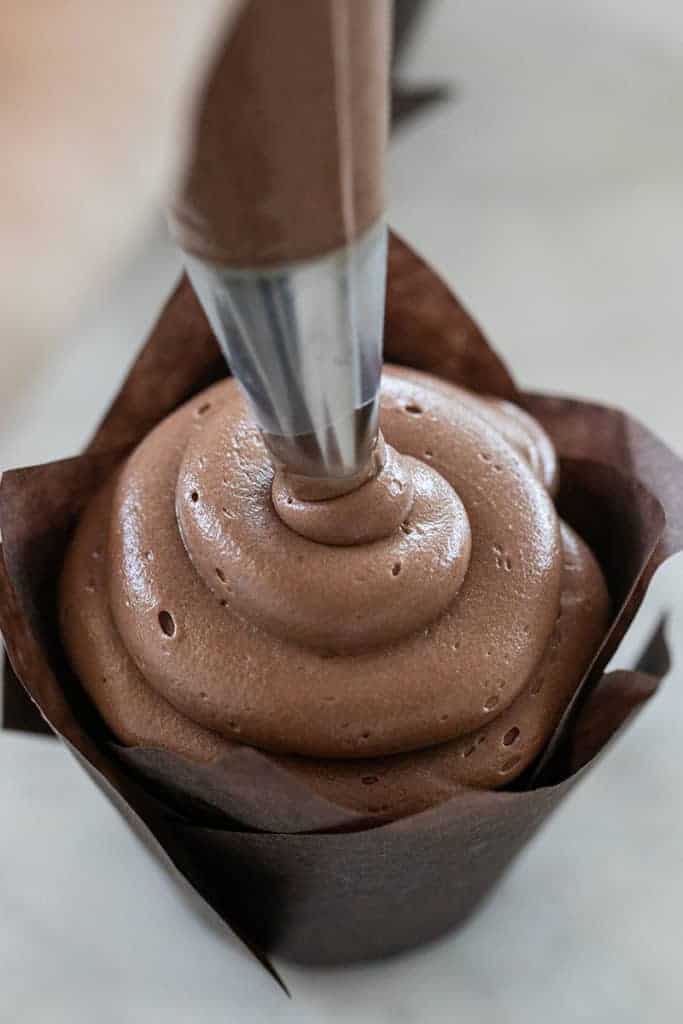 Piping chocolate buttercream on a cupcake.