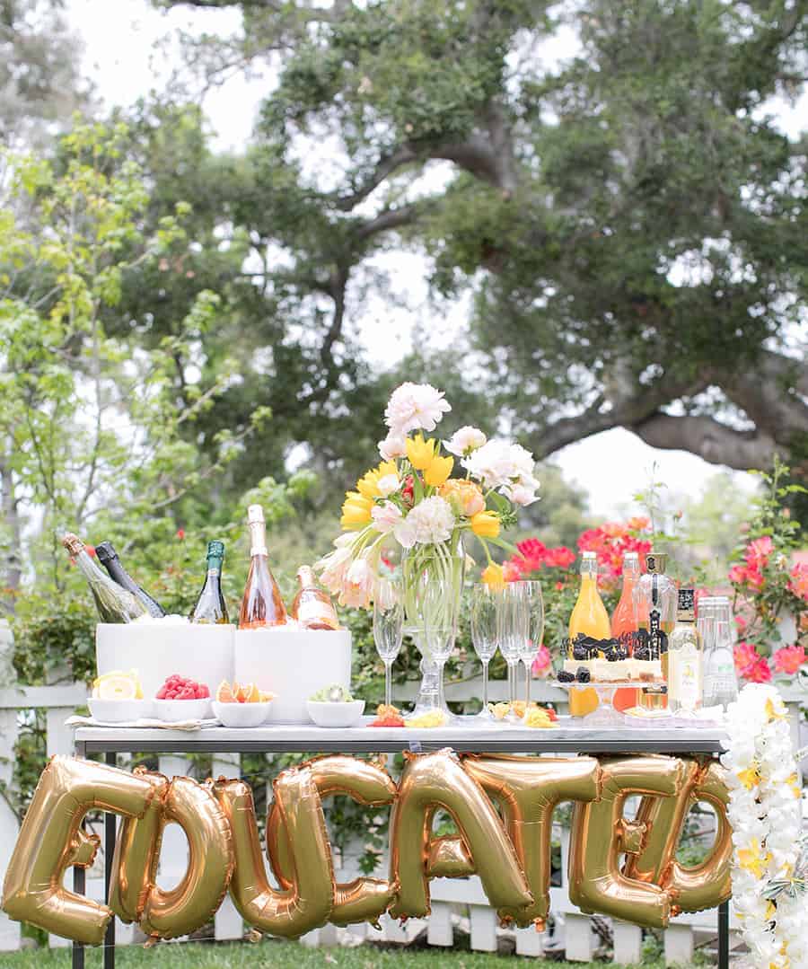 Champagne bubble bar with balloons that spell EDUCATED and flowers. - graduation party ideas