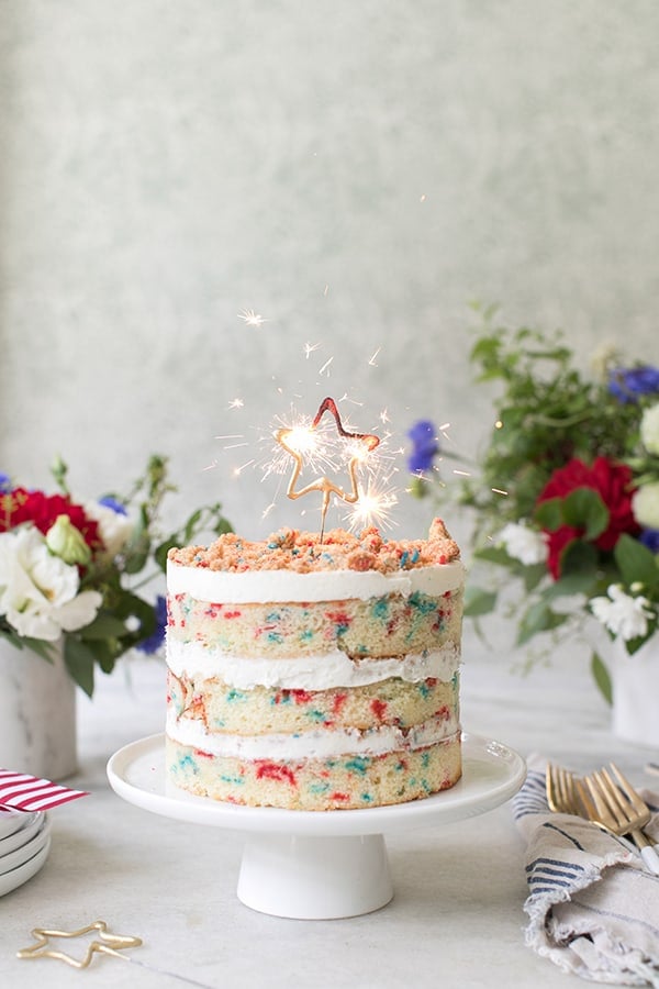 4th of July, red white and blue cake with a star sparkler lit and flowers. 