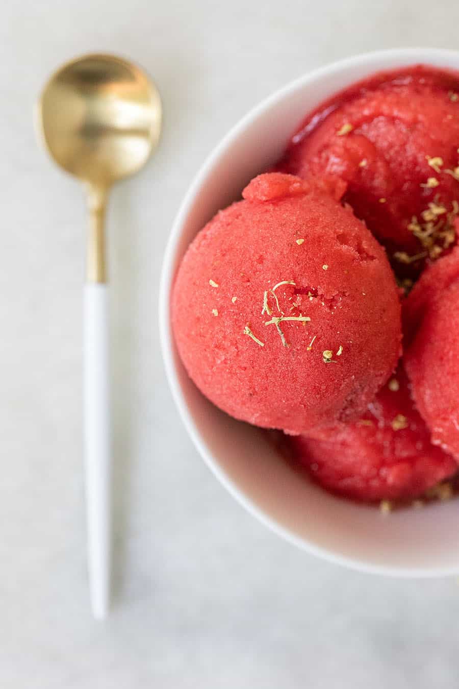 Scoops of strawberry sorbet in a white bowl with elderflower sprinkled over the top.