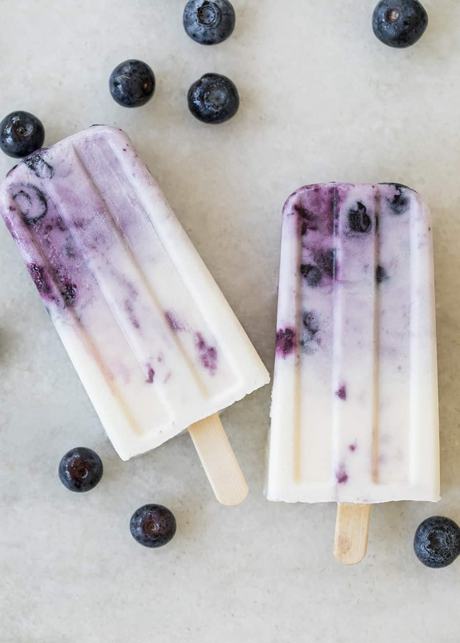 Homemade popsicles with blueberries on a marble table.