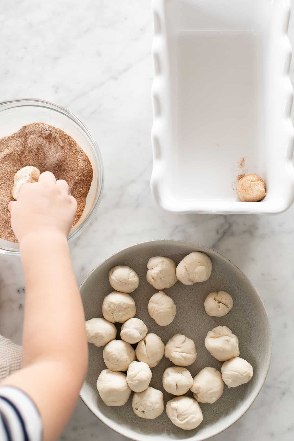 Kids making easy monkey bread by rolling small dough balls into butter, cinnamon and sugar.