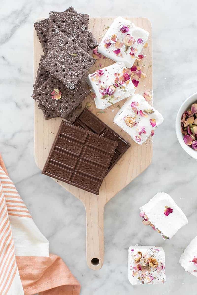 Cutting board with chocolate, giant marshmallows and rose petals.