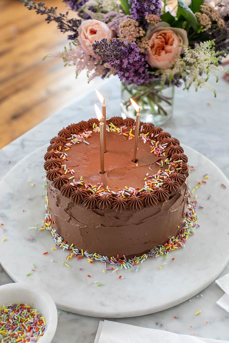 Chocolate birthday cake with candles, sprinkles and flowers.