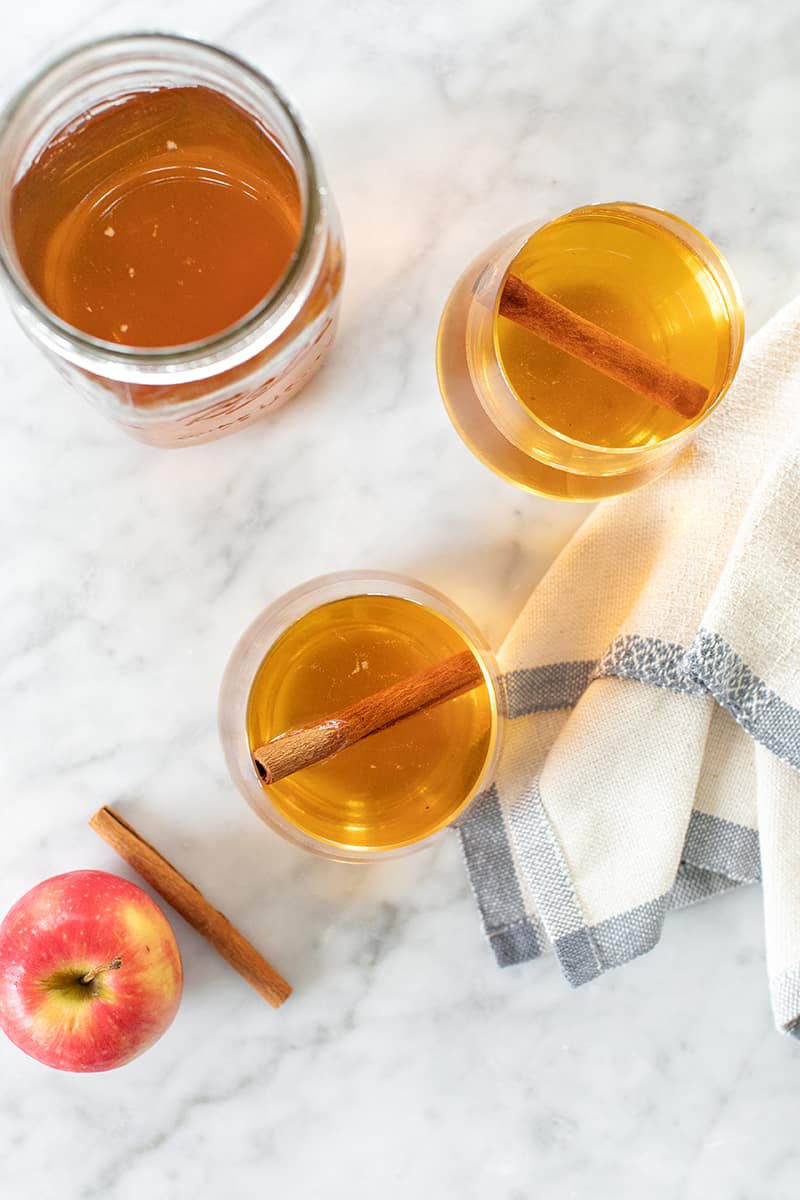 Two cups apple pie moonshine with cinnamon sticks and a jar of moonshine.