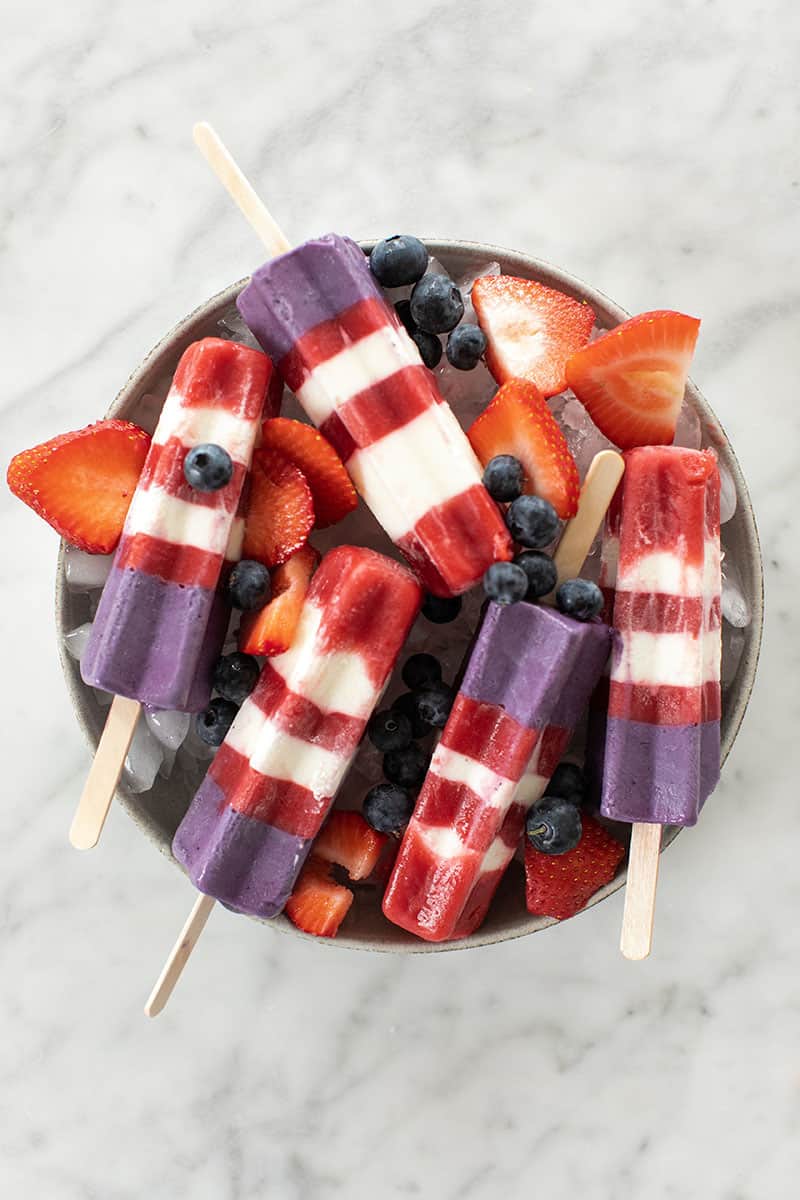 Strawberry and blueberry popsicles striped on ice with strawberries and blueberries.