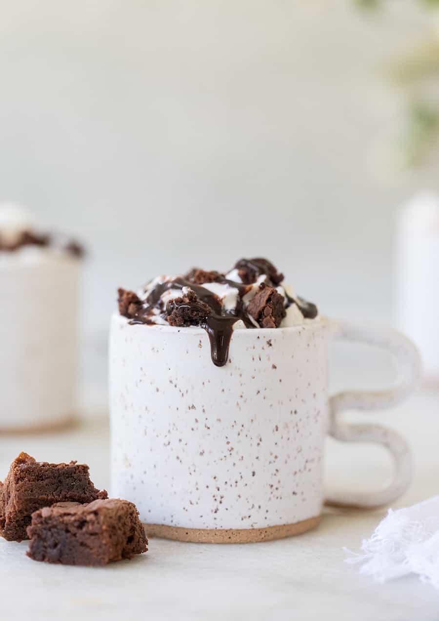 Coffee in a white ceramic cup with whipped cream, brownies and fudge.