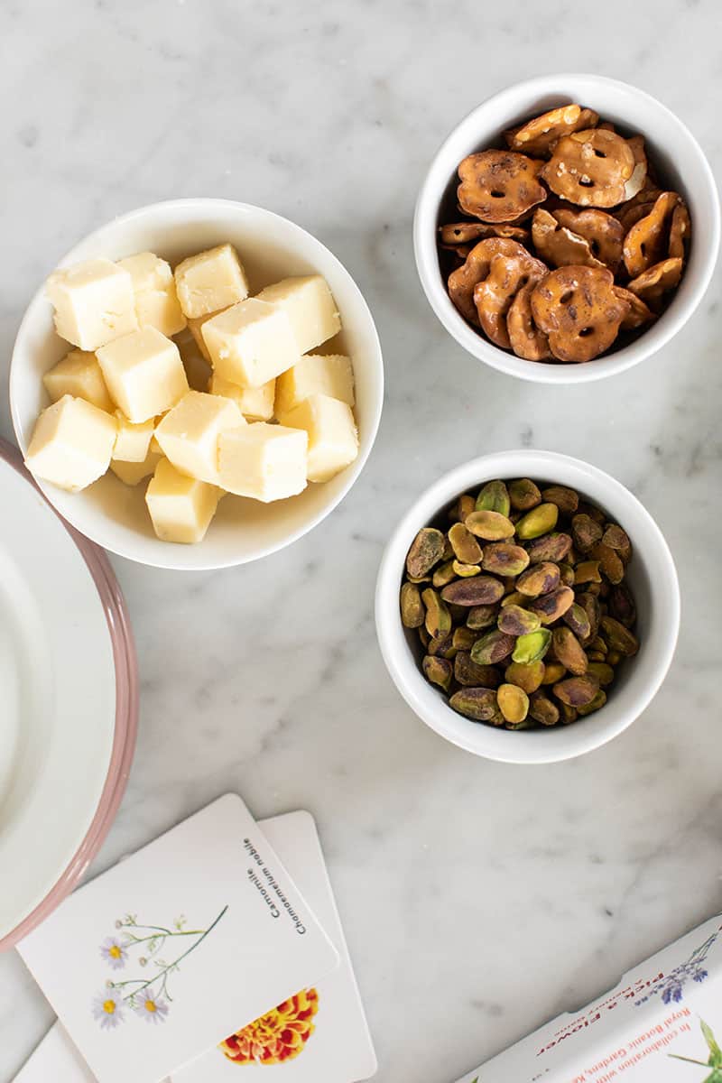 Cheese, pretzels and pistachios in small white bowls. 