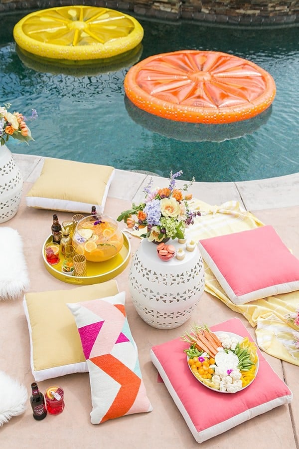 Pool party with citrus floats, pink and yellow cushions and flowers.