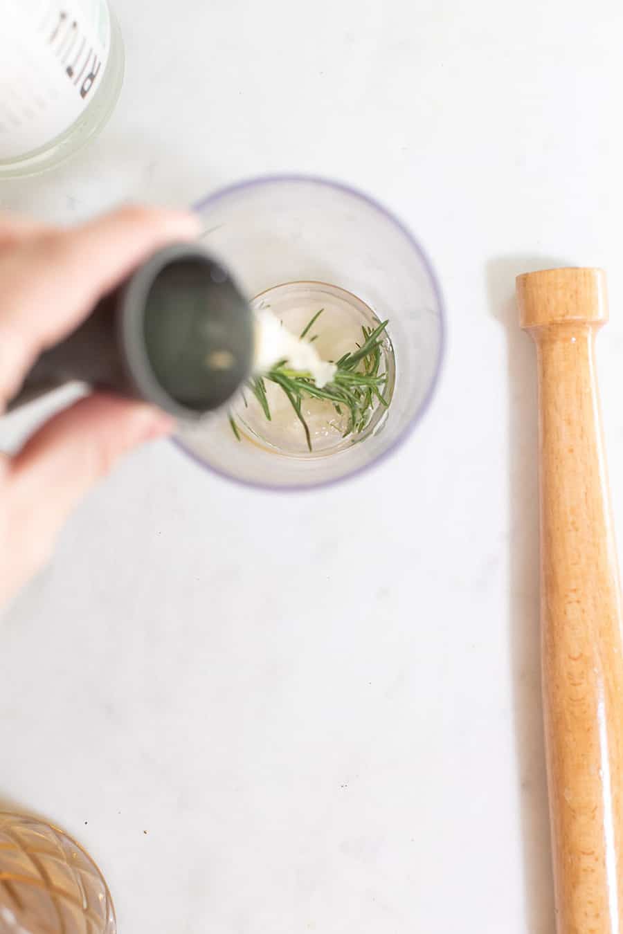 Pouring lemon juice into a cocktail shaker with rosemary.