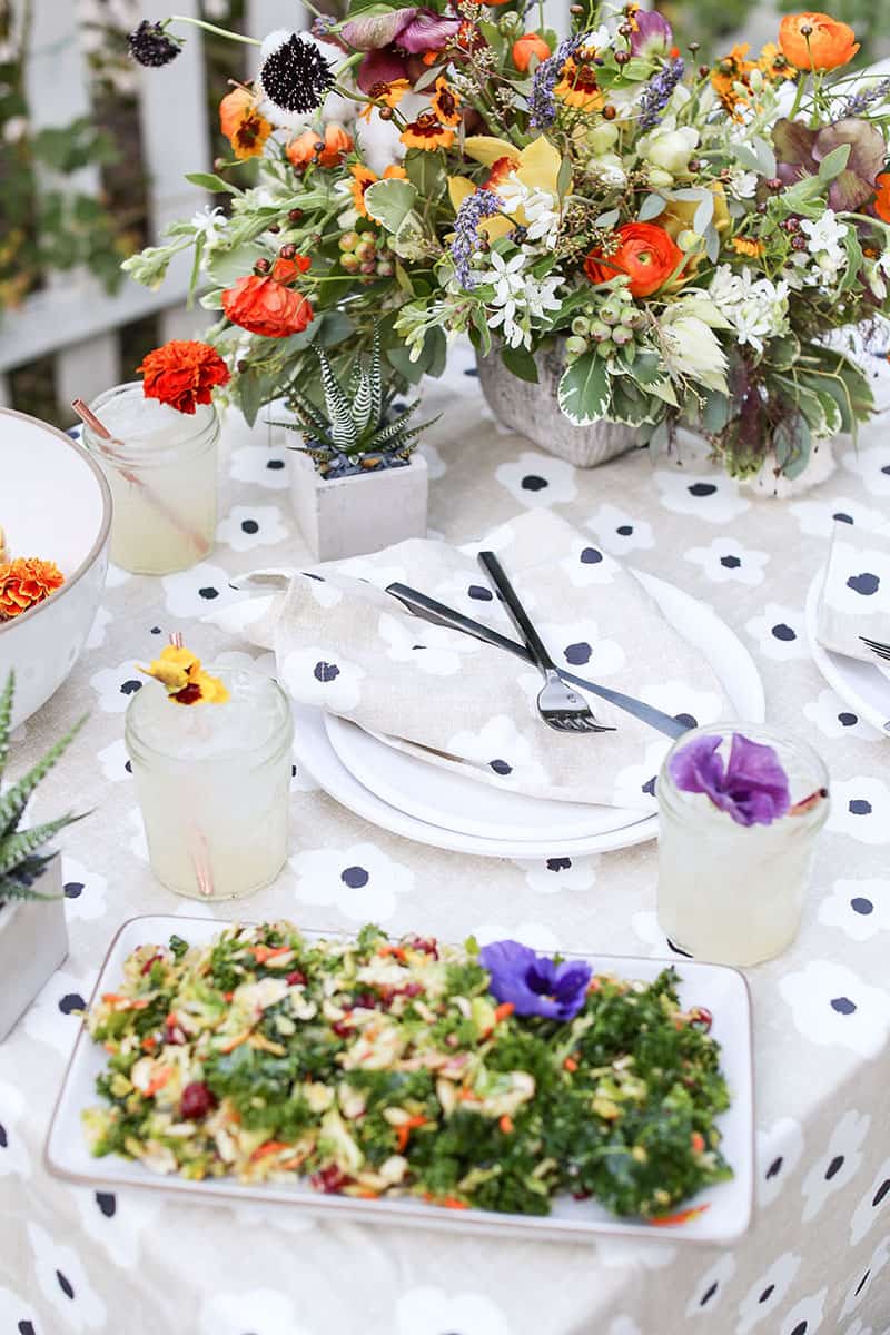 Mesa puesta en el exterior con flores y un mantel para cenar al aire libre