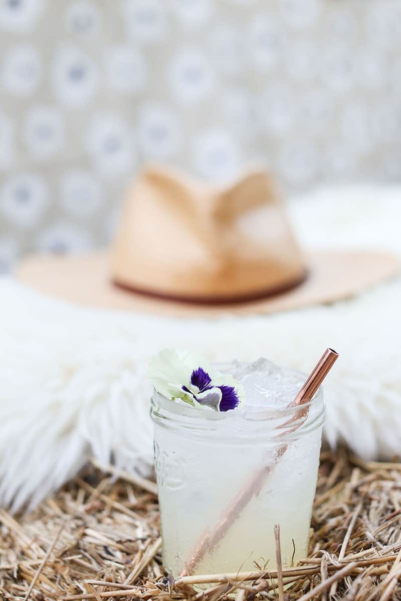 Spiked lemonade with a copper straw and a hat in the back.