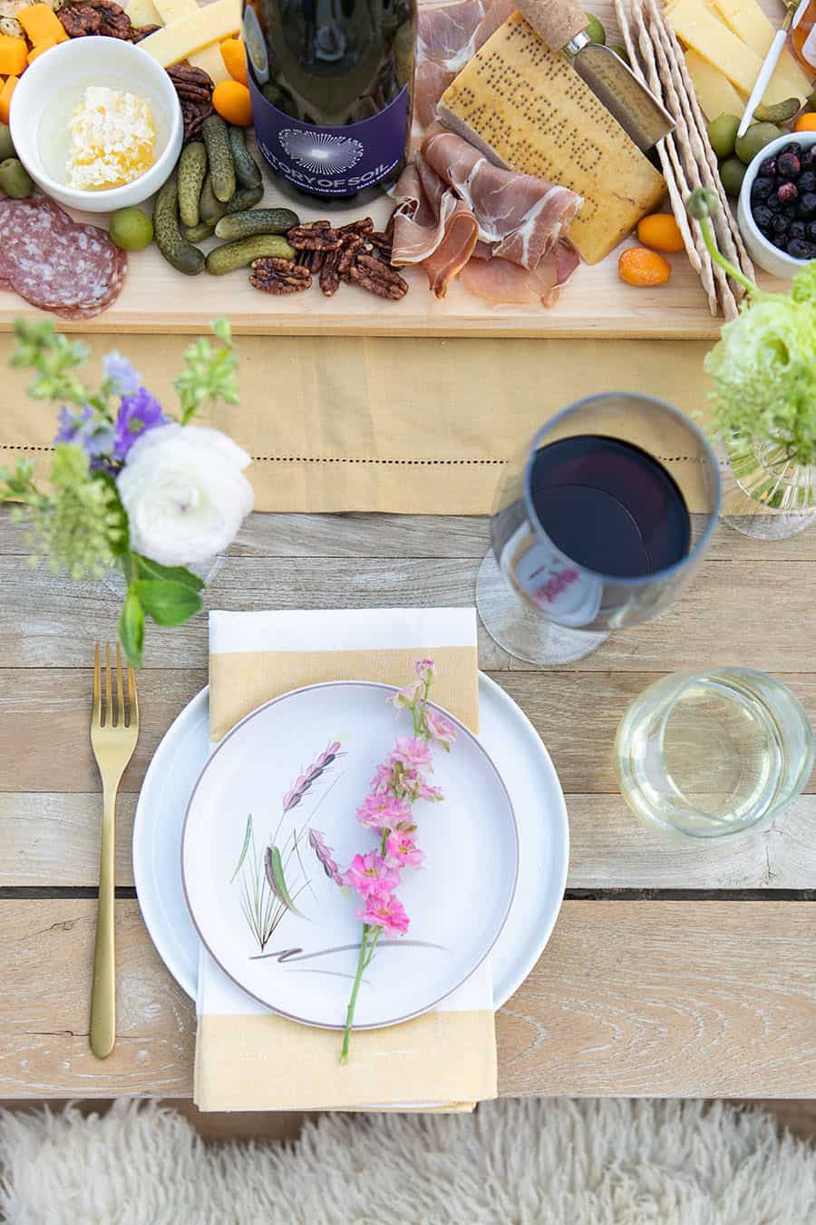 Conjunto de mesa para jantar ao ar livre com copo de vinho, pratos brancos, guardanapos às riscas e flores.