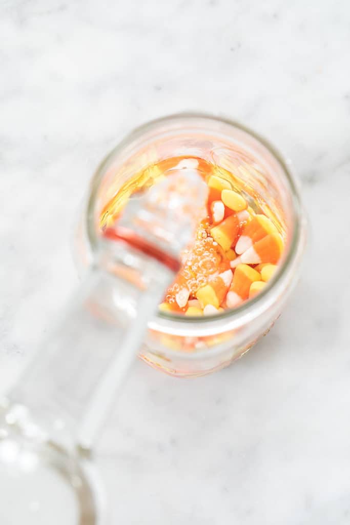 Pouring vodka into a jar filled with candy corns.
