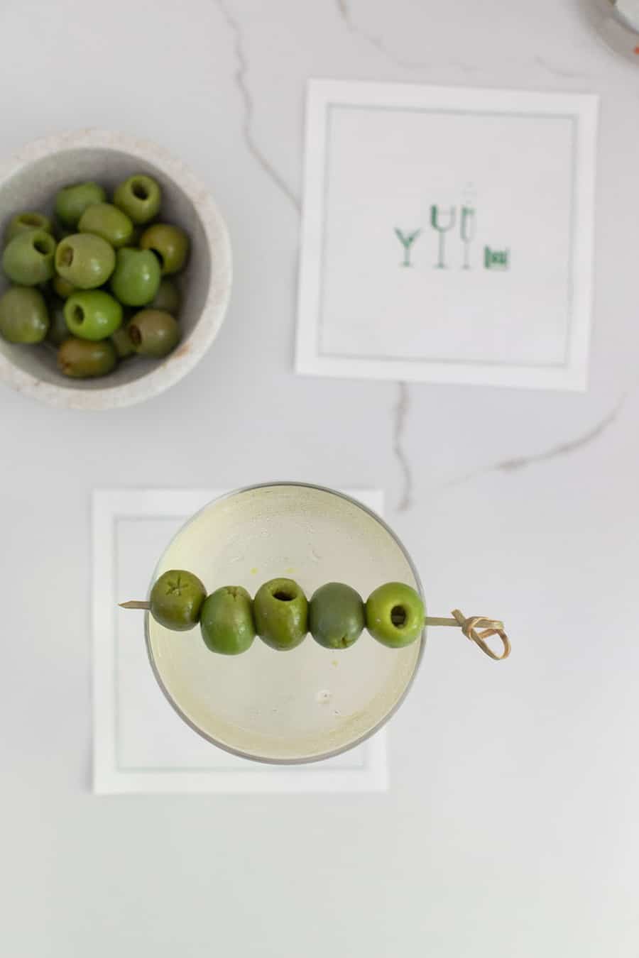 Dirty martini on a cocktail napkin with a bowl of olives